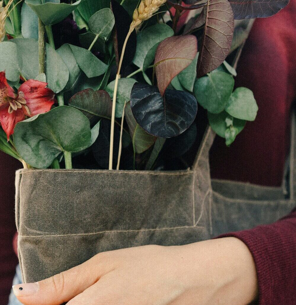 Person holding a bouquet of perennial flowers in a textured bag