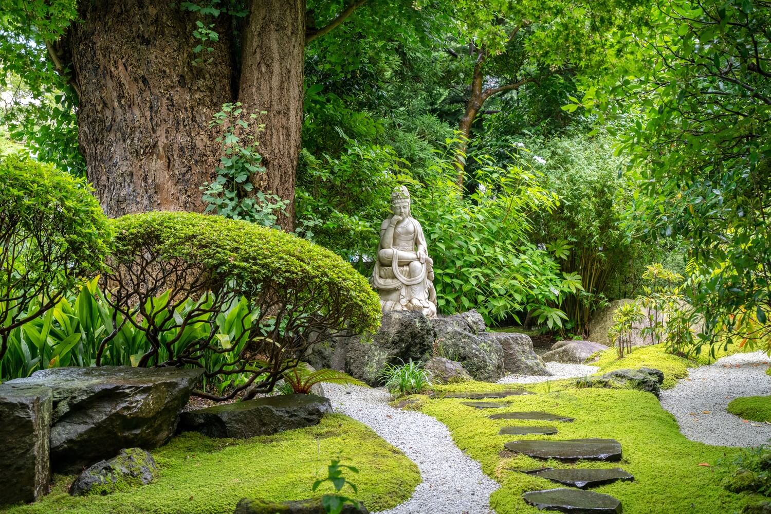 Statue of a figure in a Moss garden with stone pathways and greenery