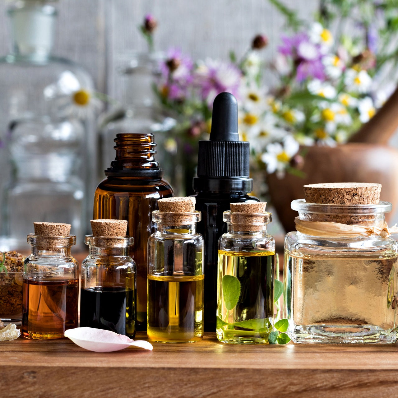 Collection of glass bottles with cork lids on a wooden surface, with a blurred floral background.